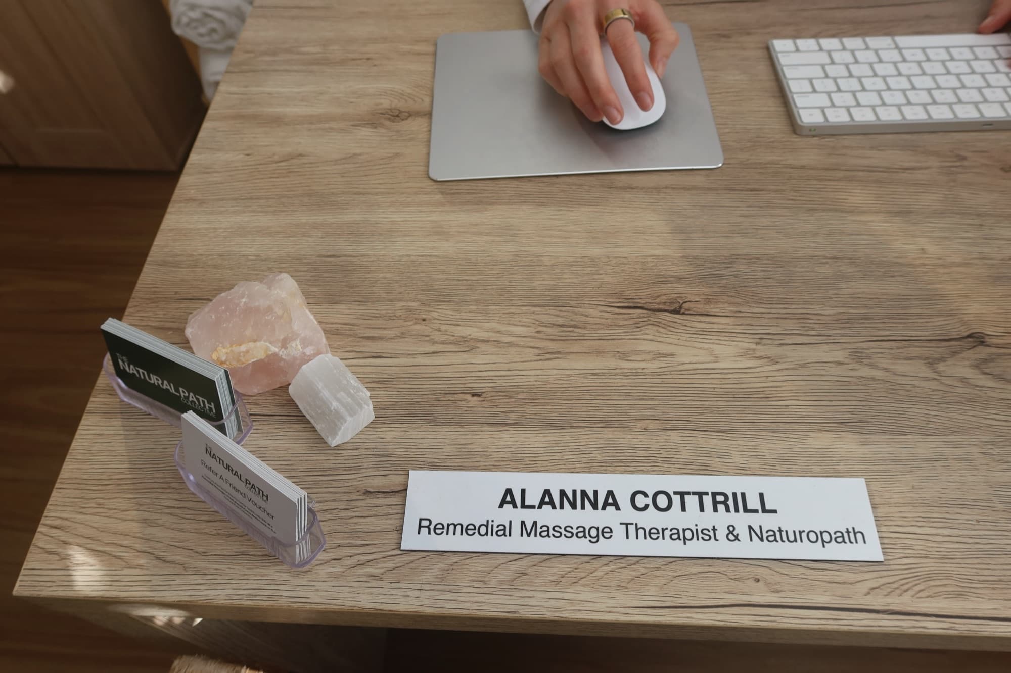 Alanna's desk at the clinic: a nameplate reading Alanna Cottrill, Remedial Massage Therapist and Naturopath, beside business cards and a piece of rose quartz.