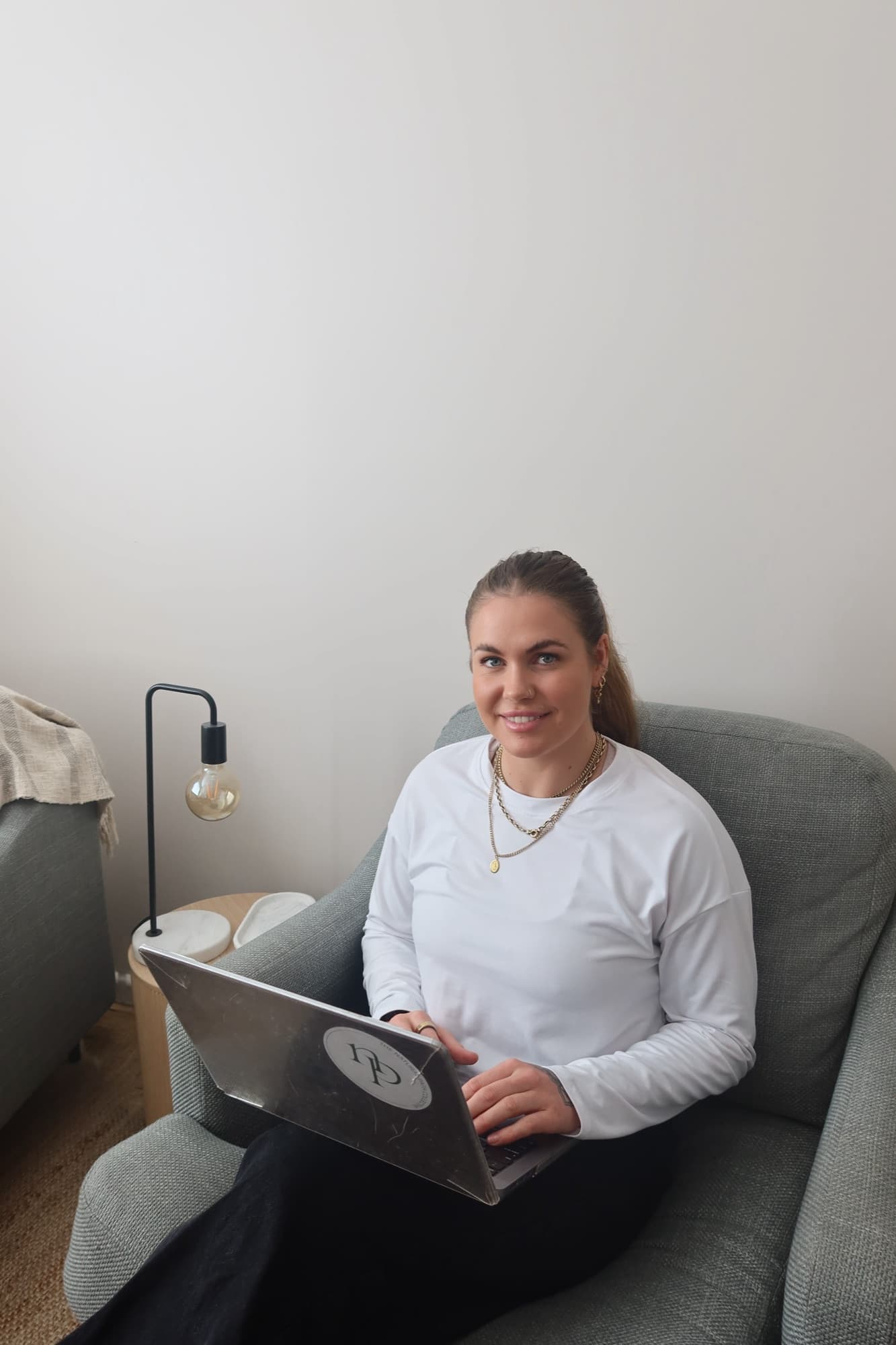 Alanna Cottrill sitting in a grey armchair with a laptop on her lap, smiling towards the camera.